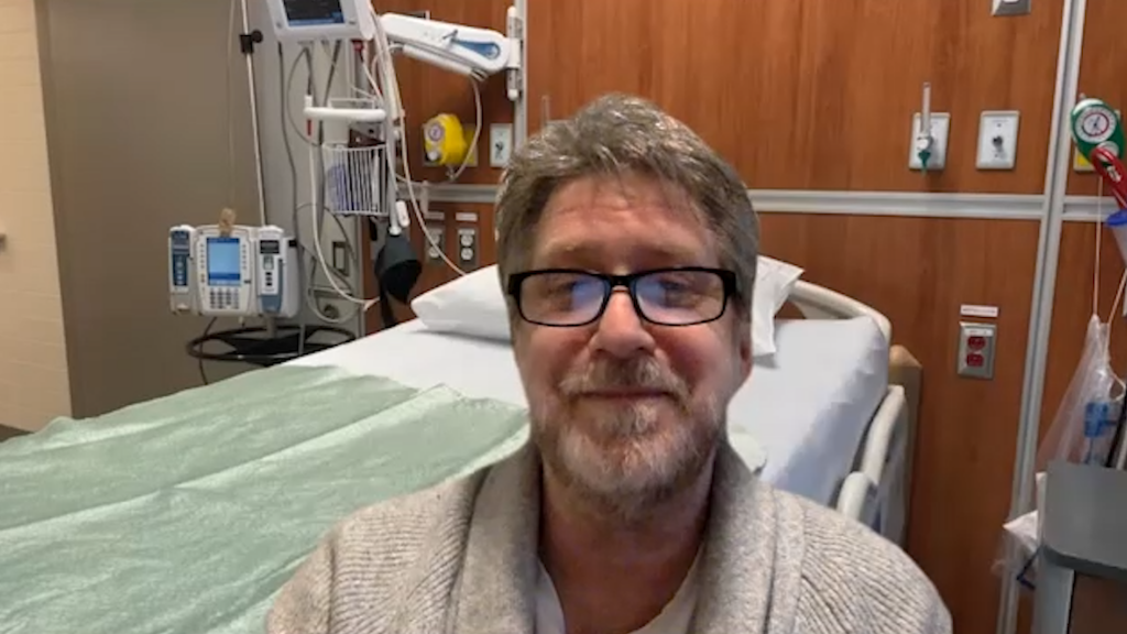 Raymond Zetner, our case study patient. Raymond wears glasses and gives a closed-mouth smile as he sits by his bed in the hospital.