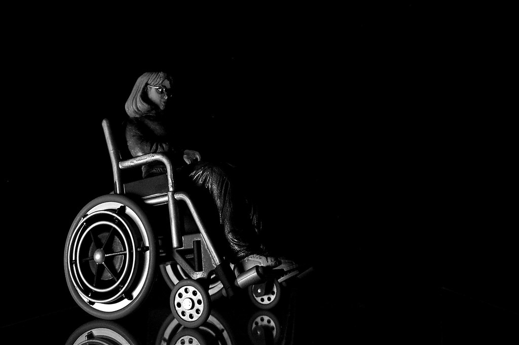A black and white photo of a figurine of oracle, a woman with medium length hair in a sleek wheelchair.