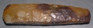 A beige and brown axe head made from flint. The surface appears to be chipped most likely from a process called knapping.